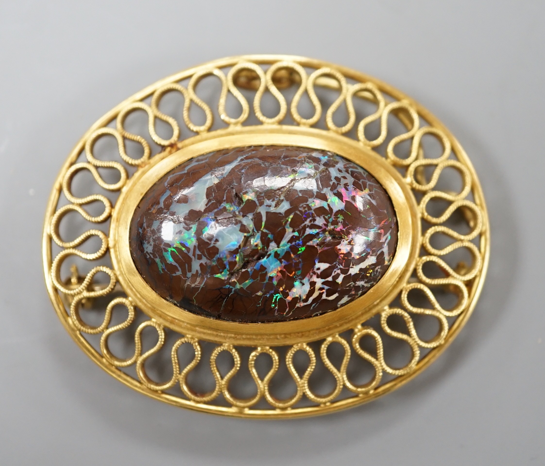 A continental 750 yellow metal and large oval boulder? opal set pendant brooch, with a filigree scroll border, 47mm, gross weight 20 grams (opal cracked).